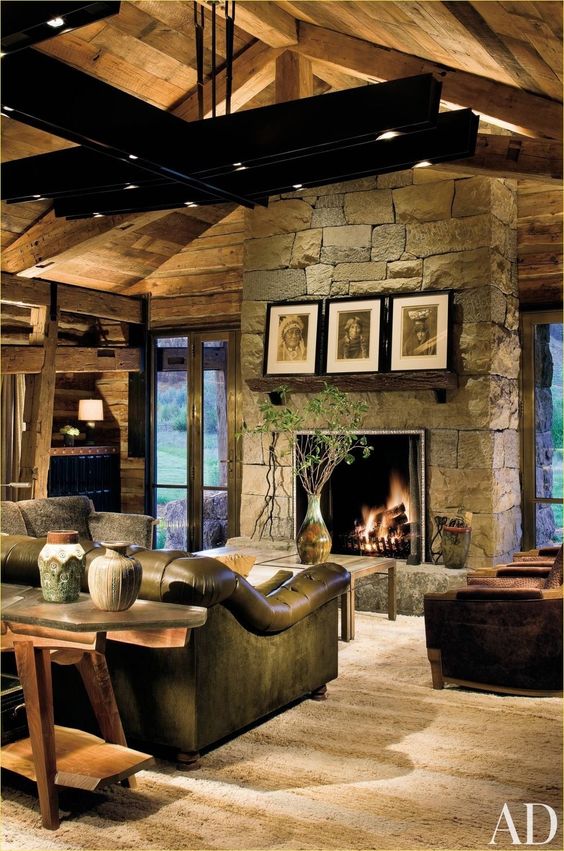 a dark rustic living room with a stone clad fireplace, wooden beams on the ceiling and leather furniture that make the space cozier