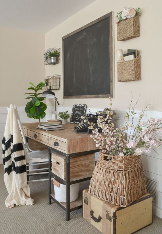 a farmhouse home office with a wooden desk, a chalkboard, baskets on the wall, a basket with flowers on a suitcase