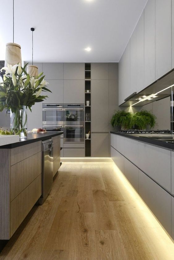 A grey minimalist kitchen with sleke cabinets, black countertops, built in lights and pendant lamps