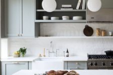 a grey vintage-inspired kitchen with paneled cabinets, white tiles and countertops and pendant lamps