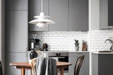 a laconic minimalist kitchen with grey sleek cabinets, a wooden dining set, a pendant lamp and additional lights