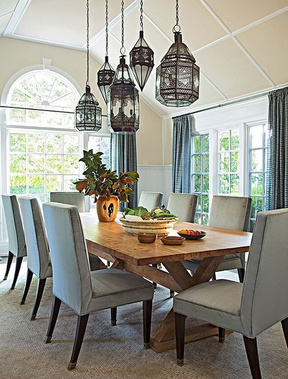 a lovely blue dining room with paneling on the walls, a wooden trestle table and pale blue chairs plus a cluster of pendant Mrooccan lamps