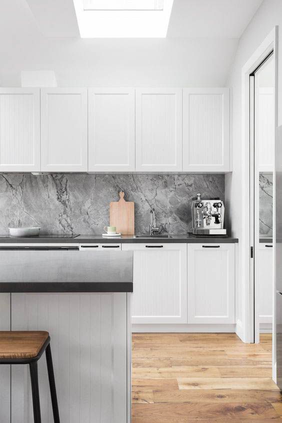 a minimal Nordic kitchen with white paneled cabinets, a grey stone backsplash, black countertops and a wooden floor
