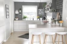 a minimalist Scandi kitchen with grey walls, sleek white cabinets, stools and pendant lamps