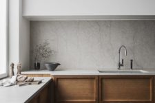 a minimalist Scandinavian kitchen with sleek white uppers, paneled wood lower cabinets, a stone backsplash and countertops