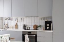 a minimalist grey kitchen, white tiles, woven chairs and a simple and small dining table