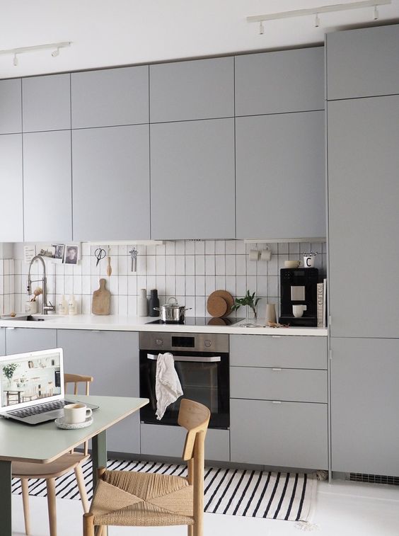 a minimalist grey kitchen, white tiles, woven chairs and a simple and small dining table
