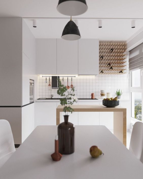 A minimalist white kitchen with built in lights, a wine bottle rack, a minimal wooden kitchen island and a white dining set