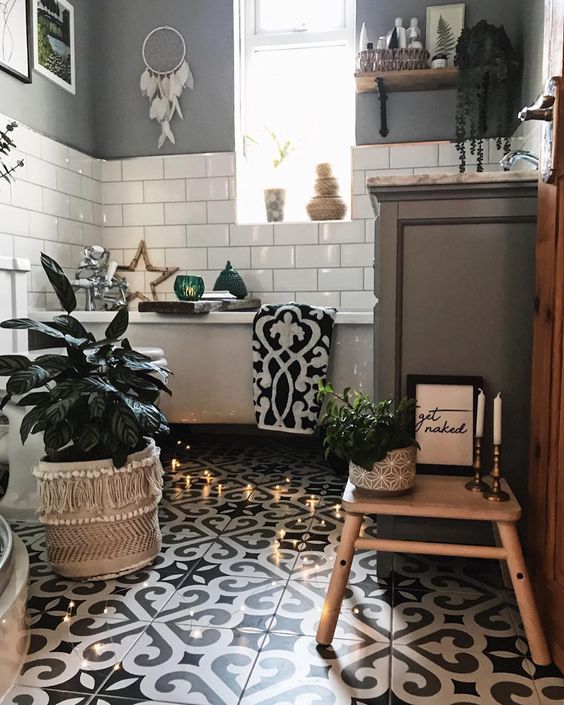 a monochromatic boho bathroom with mosaic tiles, subway white one,s a drema catcher, potted plants, lights and a tub