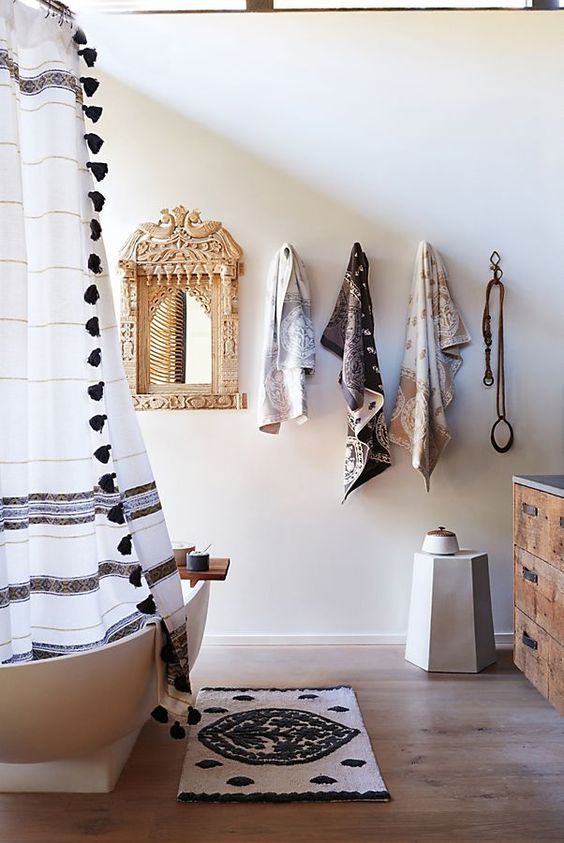 a neutral bathroom with a boho rug, a curtain with tassels, printed towels and an ornate mirror