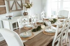 a neutral farmhouse dining room with a white sdeboard, a stained vintage table and creamy chairs, a modern chandelier for a fresh touch