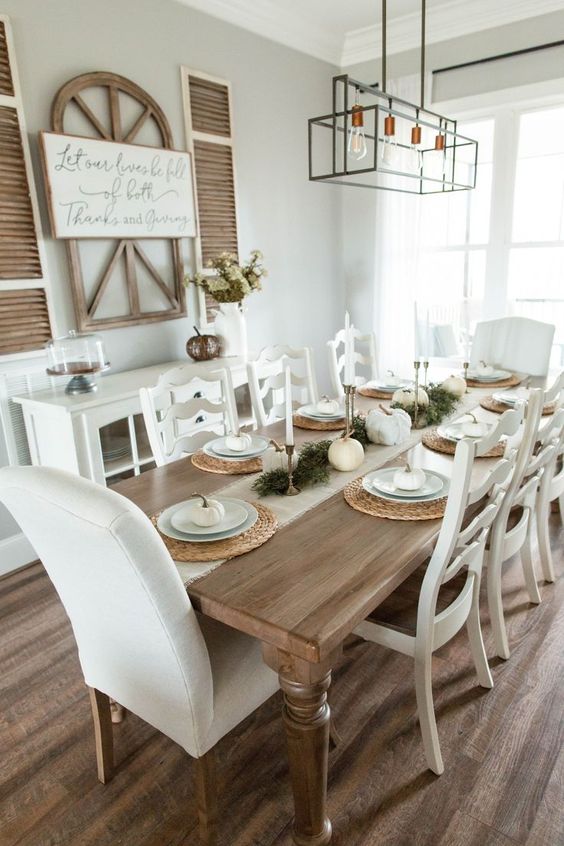 a neutral farmhouse dining room with a white sdeboard, a stained vintage table and creamy chairs, a modern chandelier for a fresh touch