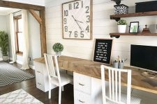 a neutral farmhouse home office with a shared desk, white chairs, open shelves, a large clock and greenery