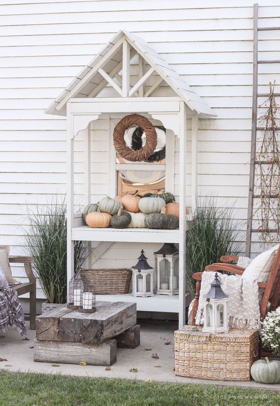 a neutral rustic patio with wooden chairs, a log table and a wicker chest plus a console with pumpkins