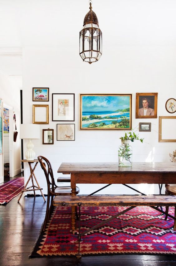 a pretty dining space with a wooden table, chairs and a bench, a bright gallery wall, a Moroccan lamp and a bright rug on the floor