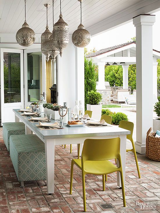 a pretty outdoor dining space with beautiful Moroccan pendant lamps, a long table with printed poufs and bright chairs