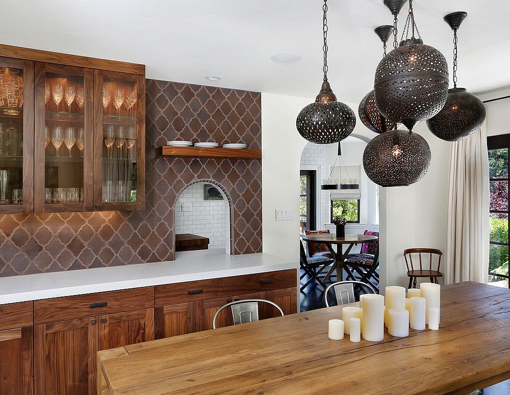 a refined eat-in kitchen with dark stained cabinets, a brown Moroccan tile backsplash, a wooden table and metal pendant lamps over it