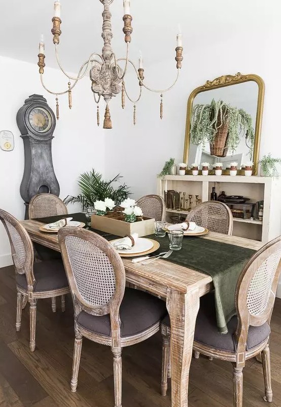a refined rustic vintage dining room with a credenza, a large mirror, lots of greenery and an elegant stained dining set plus a vintage chandelier