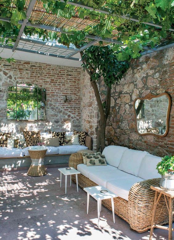 a rustic Spanish terrace with wicker furniture and printed pillows, white tables and greenery and trees