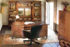 a rustic home office with a rough wooden ceiling, heavy wooden furniture, a vintage rug, a leather chair and some lamps