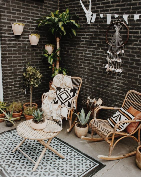 a small and cozy boho patio with rattan furniture, a dream catcher with crystals, a printed rug and pillows and potted plants