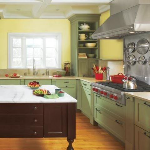 a stylish farmhouse kitchen with yellow walls, green cabinets, a dark kitchen island and a stone countertop