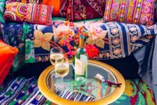 a super colorful boho space with printed pillows and rugs and a metal coffee table with a glass tabletop