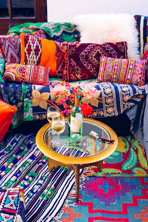 a super colorful boho space with printed pillows and rugs and a metal coffee table with a glass tabletop