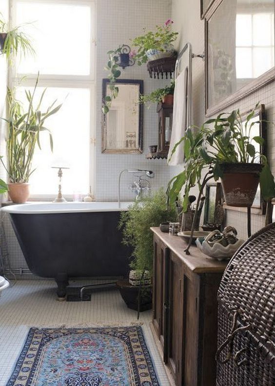 a vintage boho bathroom with a black tub, potted greenery, a stained cabinet and a boho rug