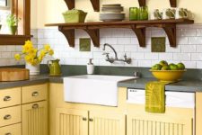 a vintage farmhouse kitchen with yellow cabinets, grey stone countertops, open shelving with green tableware and green textiles