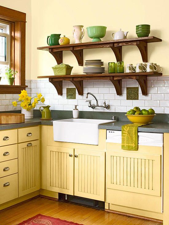 a vintage farmhouse kitchen with yellow cabinets, grey stone countertops, open shelving with green tableware and green textiles