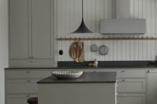 a vintage grey kitchen with elegant cabinets, black countertpos, a black pendant lamp and a shiplap wall