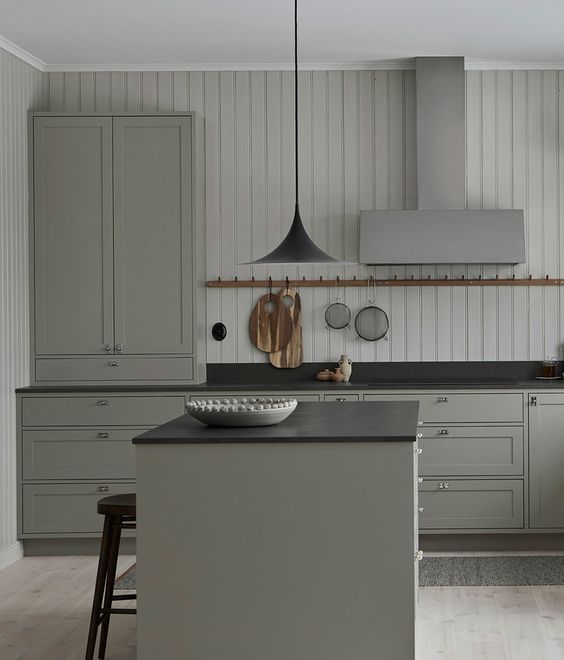 a vintage grey kitchen with elegant cabinets, black countertpos, a black pendant lamp and a shiplap wall