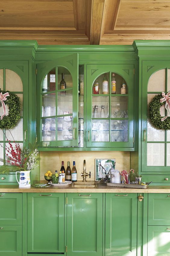 a vintage kitchen with green cabinets, tan stone countertops and a backsplash plus bold blooms