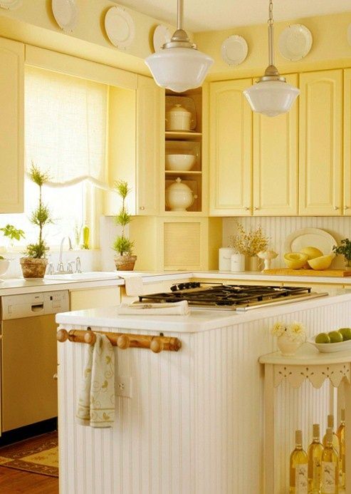 a vintage kitchen with light yellow cabinets, a beadboard backsplash and kitchen island plus potted greenery and accessories