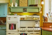 a vintage kitchen with mustard walls, vintage green cabinets, neutral appliances and pendant lamps