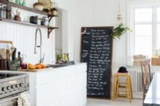 a welcoing and light-filled Nordic kitchen with shiplap walls, a white floor, a chalkboard and sleek cabinets plus lights