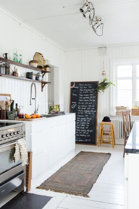 a welcoing and light-filled Nordic kitchen with shiplap walls, a white floor, a chalkboard and sleek cabinets plus lights