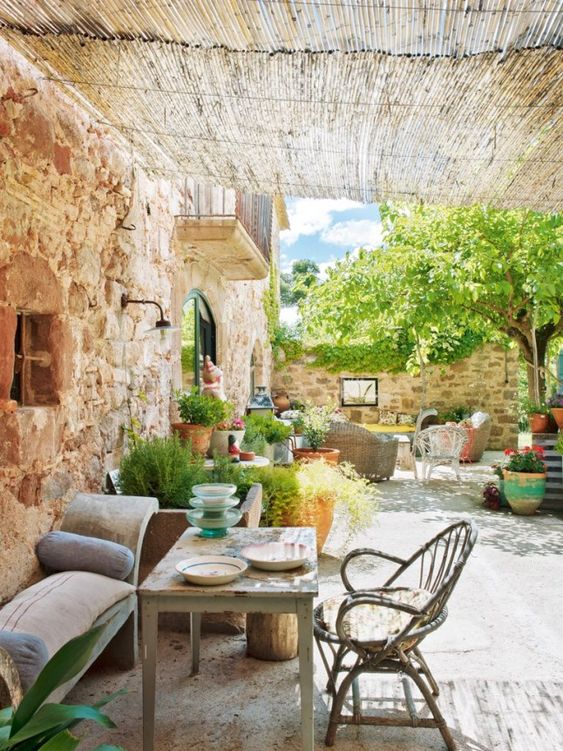 a welcoming rustic patio in Spanish style, with stone walls, rattan and wooden furniture and potted greenery and blooms