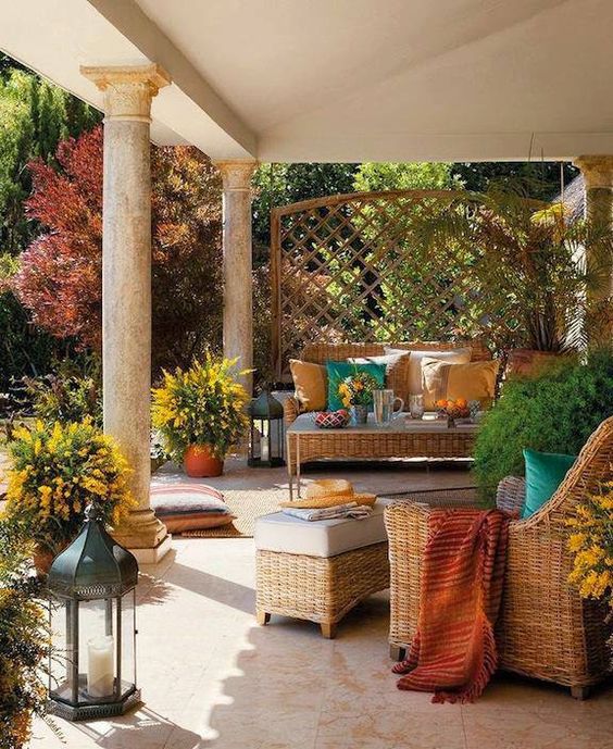 a welcoming rustic patio with neutral wicker furniture, colorful textiles, potted blooms and a trellis