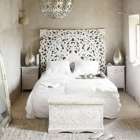 a white Moroccan bedroom with a carved headboard, chest and nightstands, silve rlanterns and a jute rug
