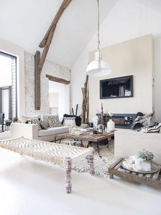 a white rustic living room with a built-in fireplace, a wooden beam with a pendant lamp, rough wood tables and a woven daybed