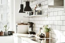 an airy kitchen with white tiles, white cabinets, wooden countertops, black pendant lamps