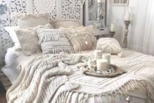 an all-white Moroccan bedroom with an ornate wodoen screen, crochet pillows and blankets, candles and lanterns and dream catchers