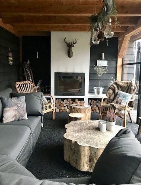 an outdoor living room with a fireplace, a deer head, a tree stump table and upholstered furniture
