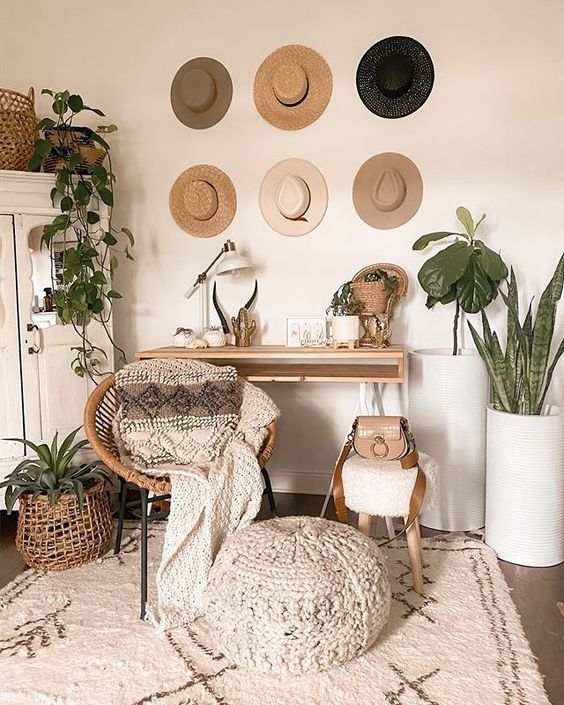 a boho chic home office with a sleek desk, a rattan chair, a wooden sotol and a woven ottoman, potted plants and hats on display