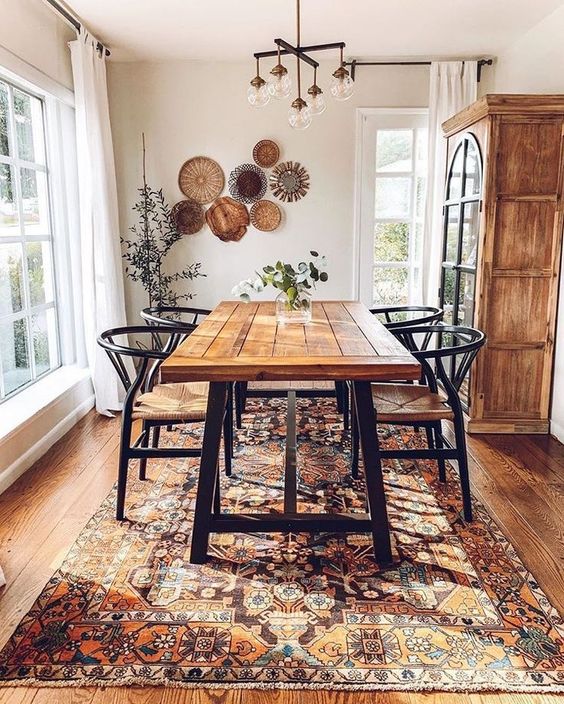 a boho dining room with a beautiful Eastern rug, an arrangement of decorative plates, a wooden table and wicker chairs