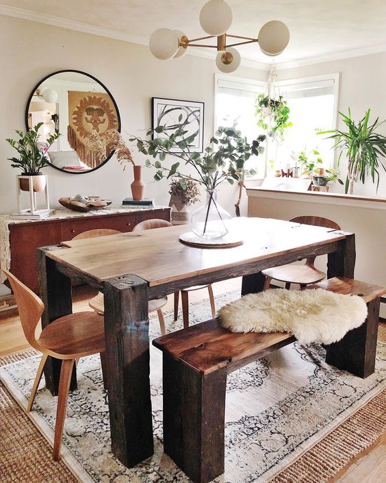 A boho dining space with a wooden set, a mid century modern chandelier, a round mirror and greenery arrangements