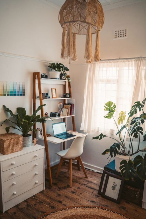 a boho home office nook with a small desk with shelves, a dresser with a basket and potted plants, a woven chandelier and a white chair