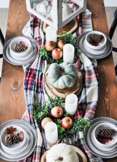 a bold fall tablescape with a plad runner, greenery, apples, heirloom pumpkins candles and pinecones